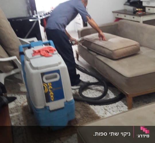 אדם מנקה ספה עם מכונת ניקוי מקצועית